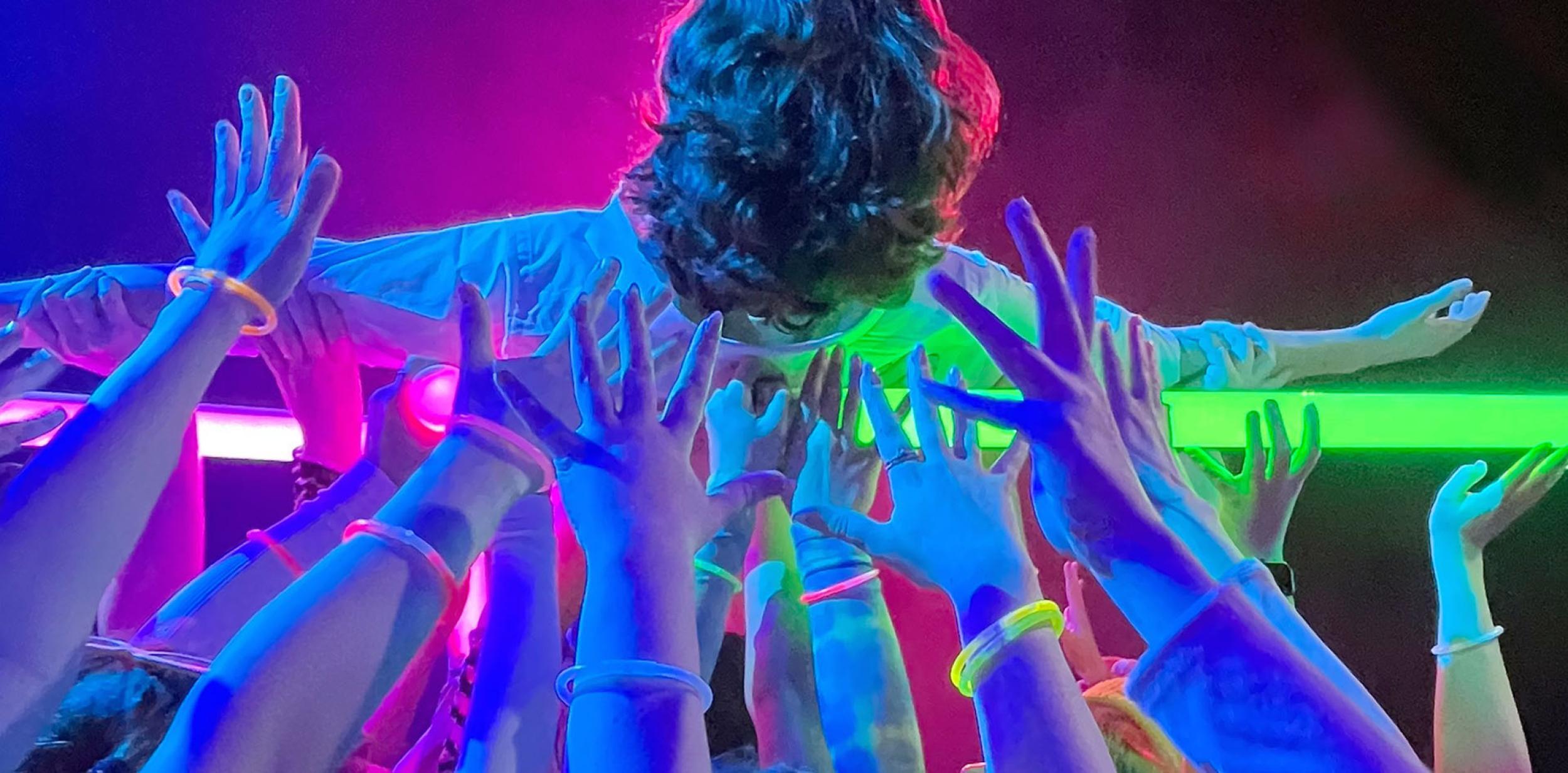 Multiple hands lifting a body, against a bright purple background