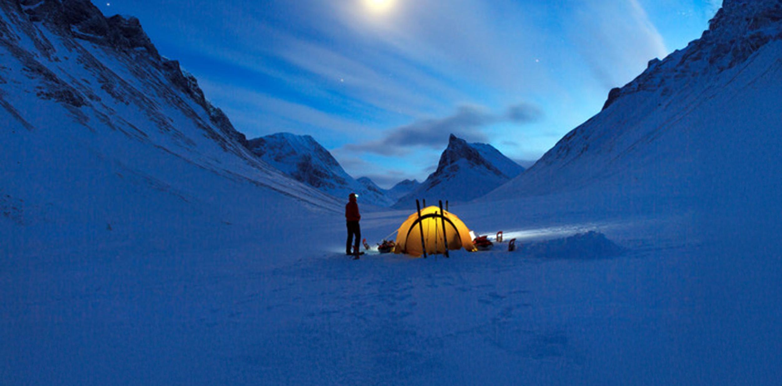 An explorer setting up a tent in a snowy valley