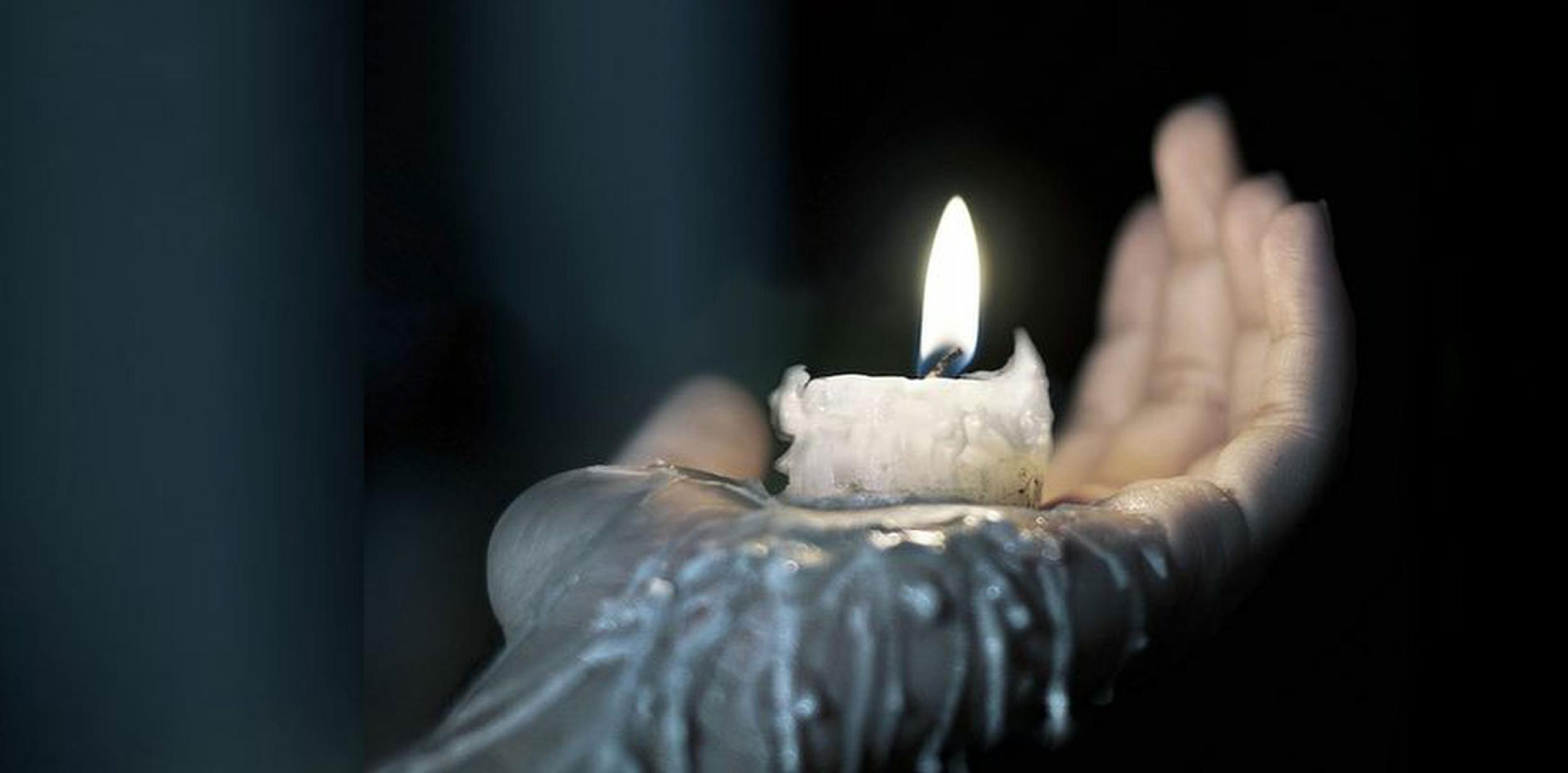 A hand holding a melting wax candle