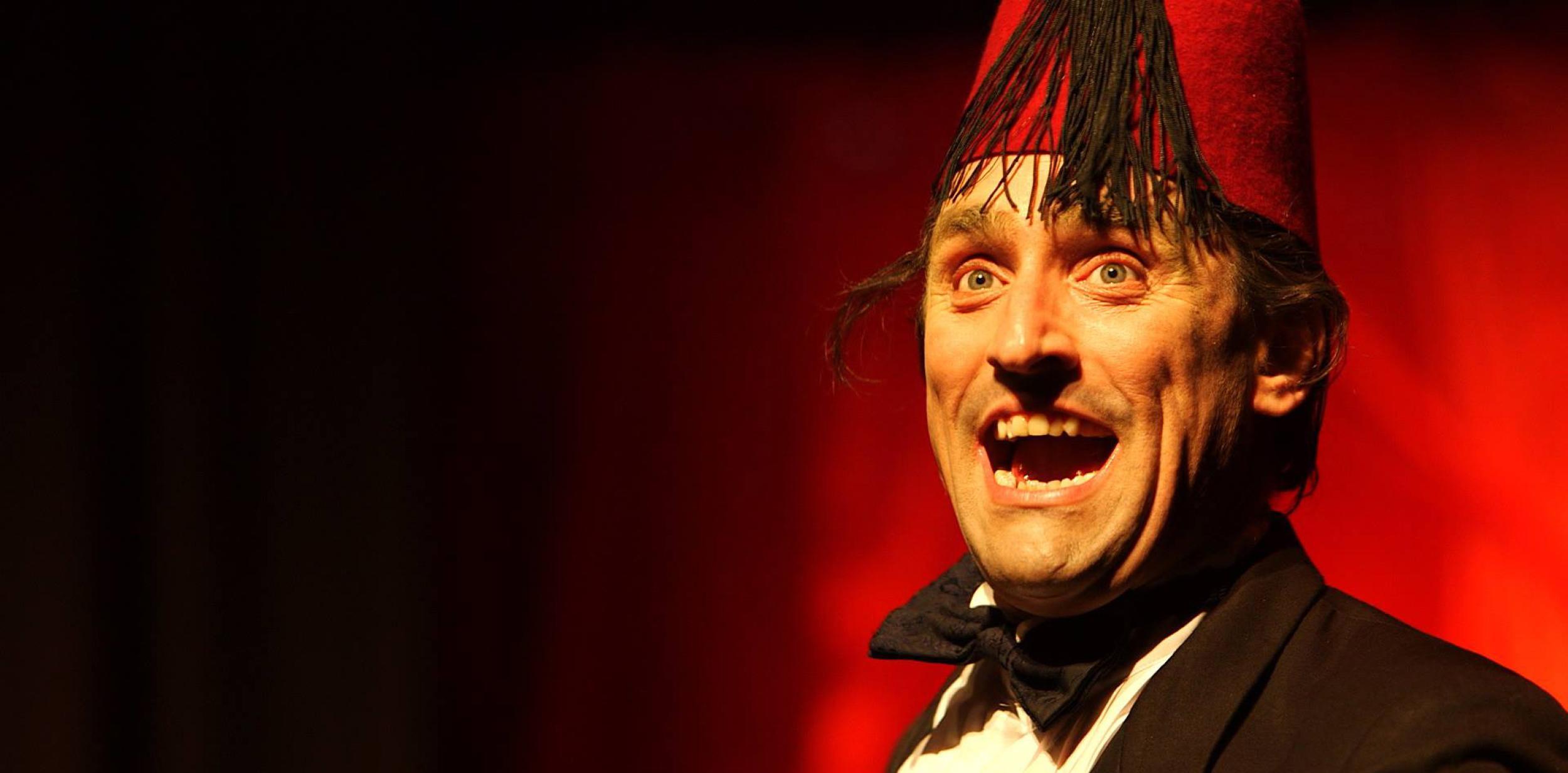 actor dressed as Tommy Cooper in black tie, black bowtie and red fez