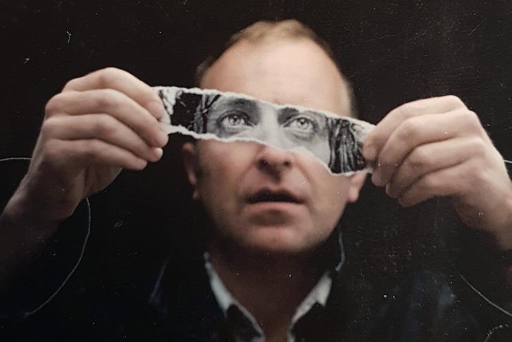 Man holding a strip of a photo over his eyes