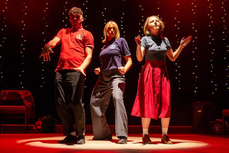 Three people dancing under a spotlight on stage