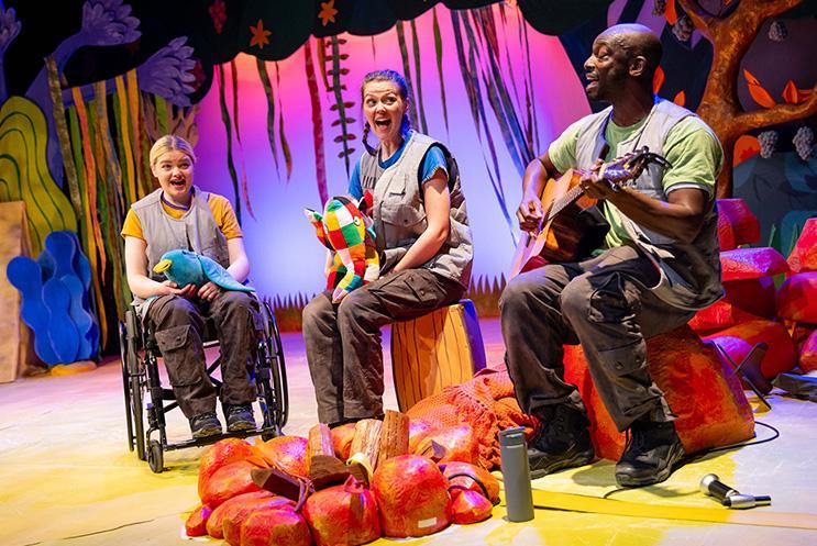 Three performers sat singing around a camp fire