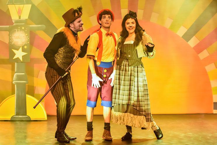 Three Pinocchio character performing on a brightly lit stage